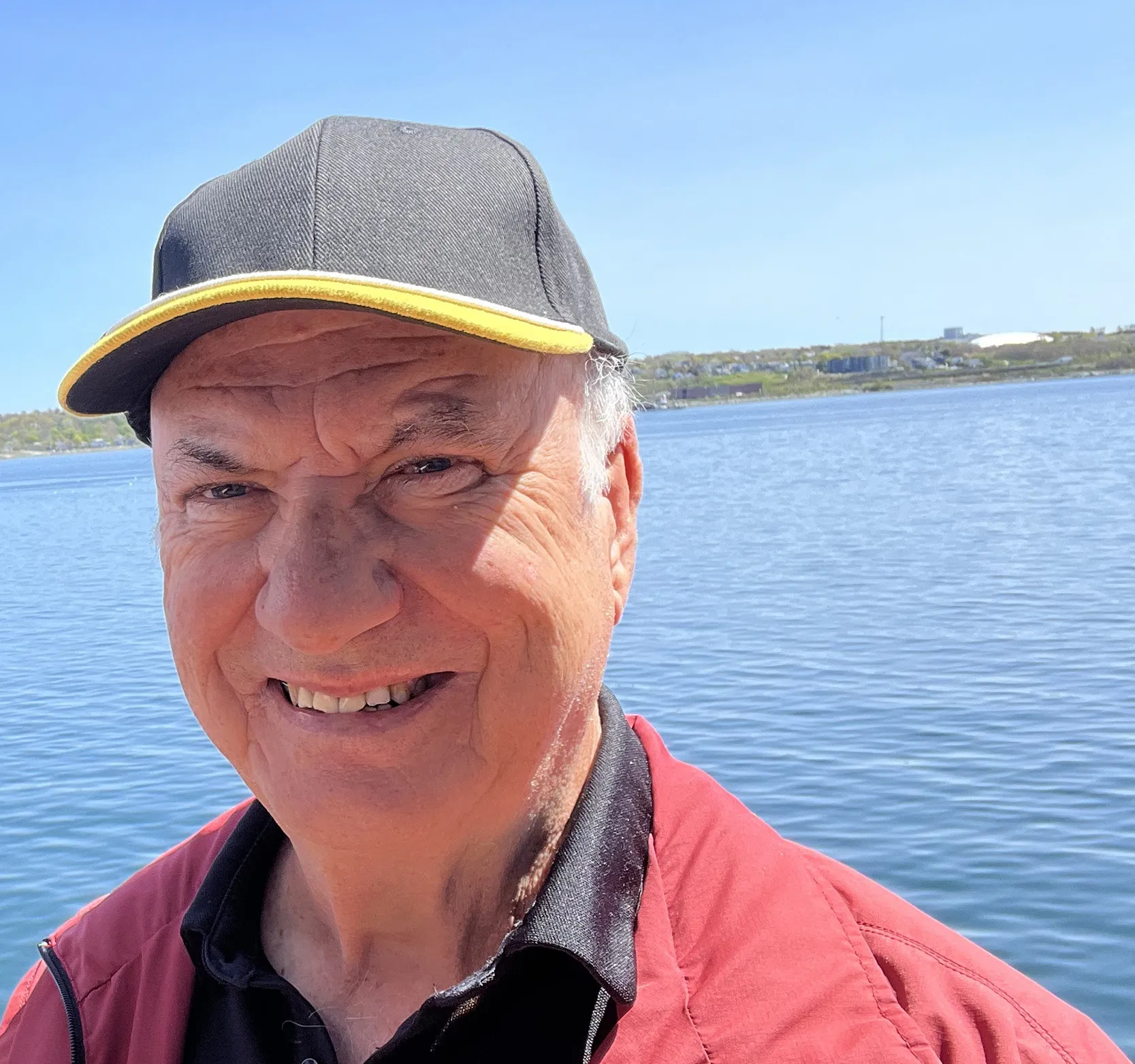 Doug Dolan stands in a red coat and blue baseball cap on the shore of the Miramichi River