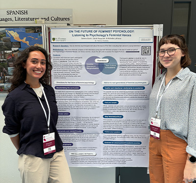 Two female ýdents smiling and standing next to poster at an academic conference