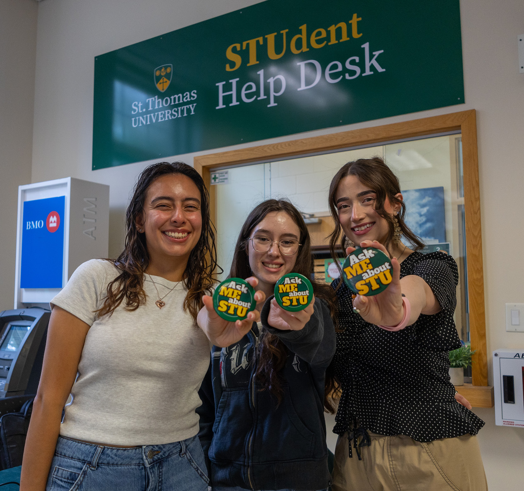 photo of three people standing in front of the STUdent Help Desk holding Ask Me About STU buttons