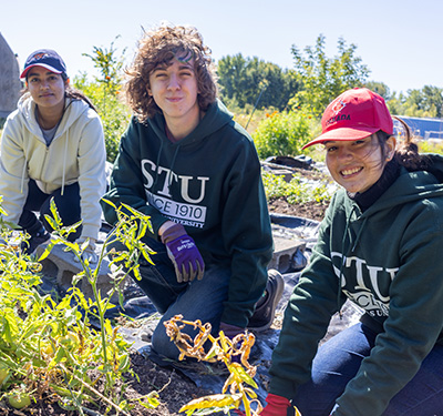 Students smiling and working in community garden outdoors with Greener Village