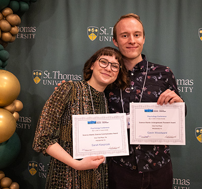 Two students in front of STU backdrop holding certificates