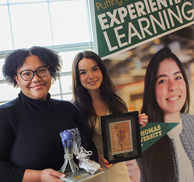 鶹dents Chante Laverlot and Jazna Ward stand together holding up their respective FutureNB and FutureWabanaki Student Excellence Awards in front of an Experiential Learning Banner.