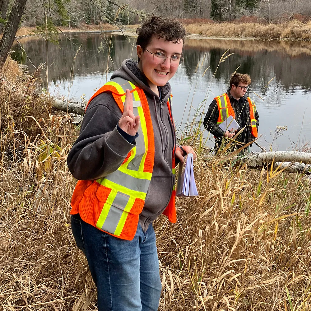 Two students stand in the marsh wearing reflective vests