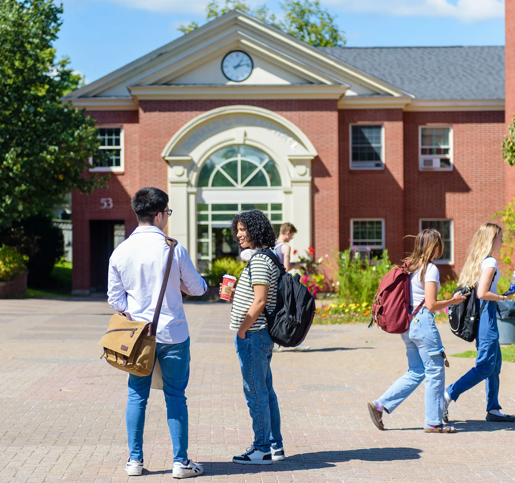 A group of students stand in the lower courtyard on campus in front of Duffie Hall