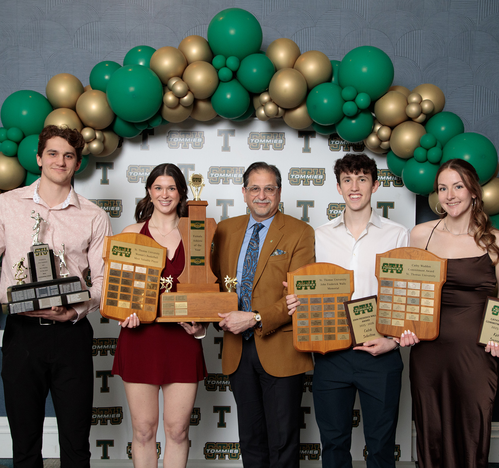 Two male students and two female students stand holding trophies and plaques with university President Dr. Nauman Farooqi
